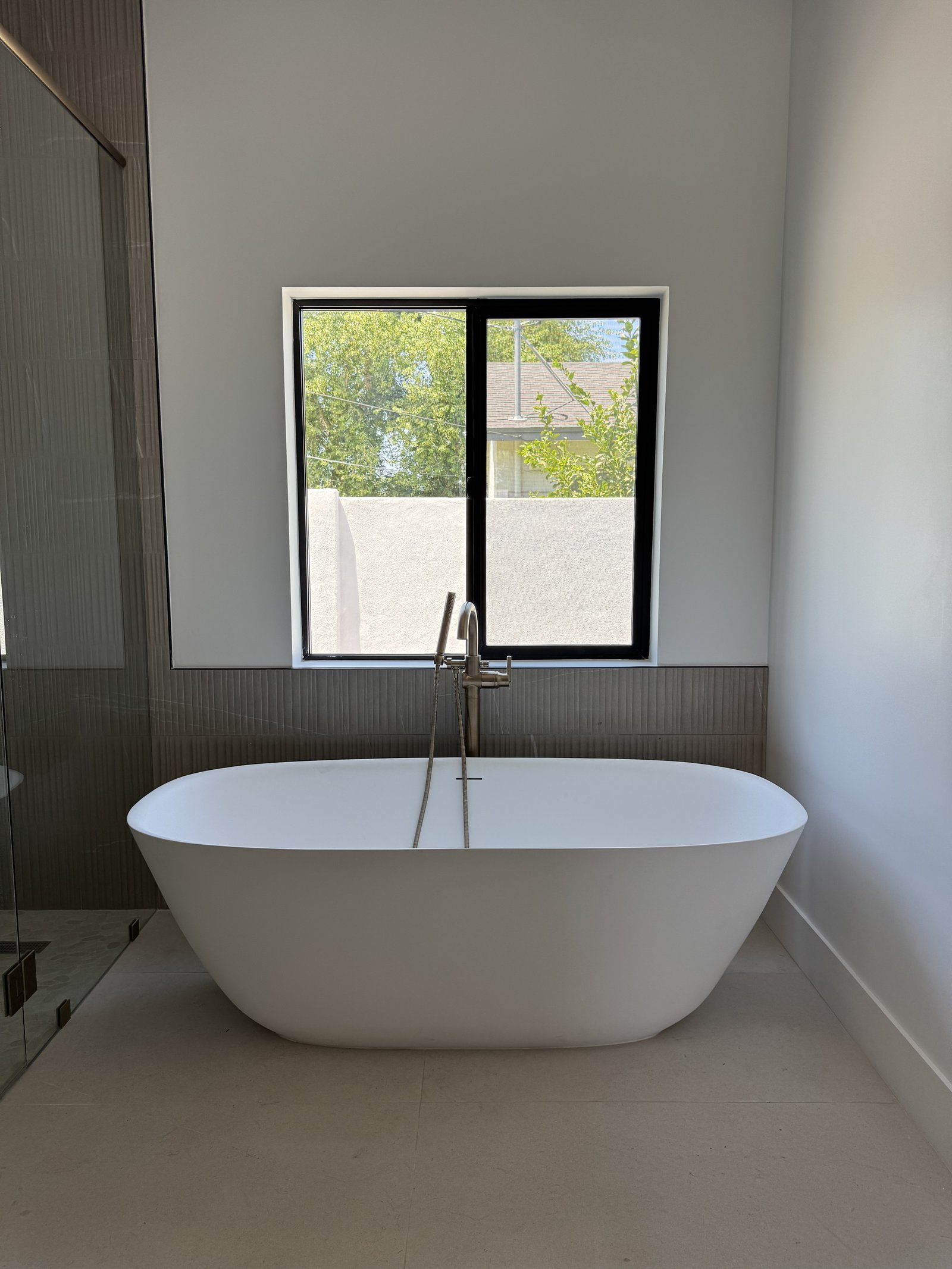 Gilbert AZ primary bathroom remodel with freestanding sculptural tub, black-framed grid window, and floor-to-ceiling gray fluted shower tile