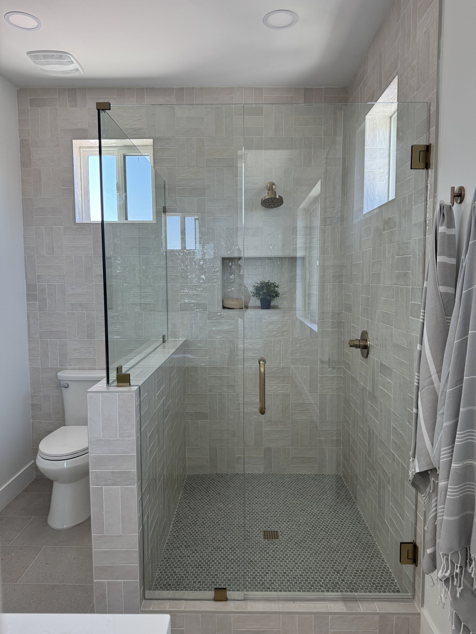 Gilbert AZ guest bathroom with light large-format tile shower, frameless glass enclosure, half-wall, brass rain head, and hex penny mosaic floor