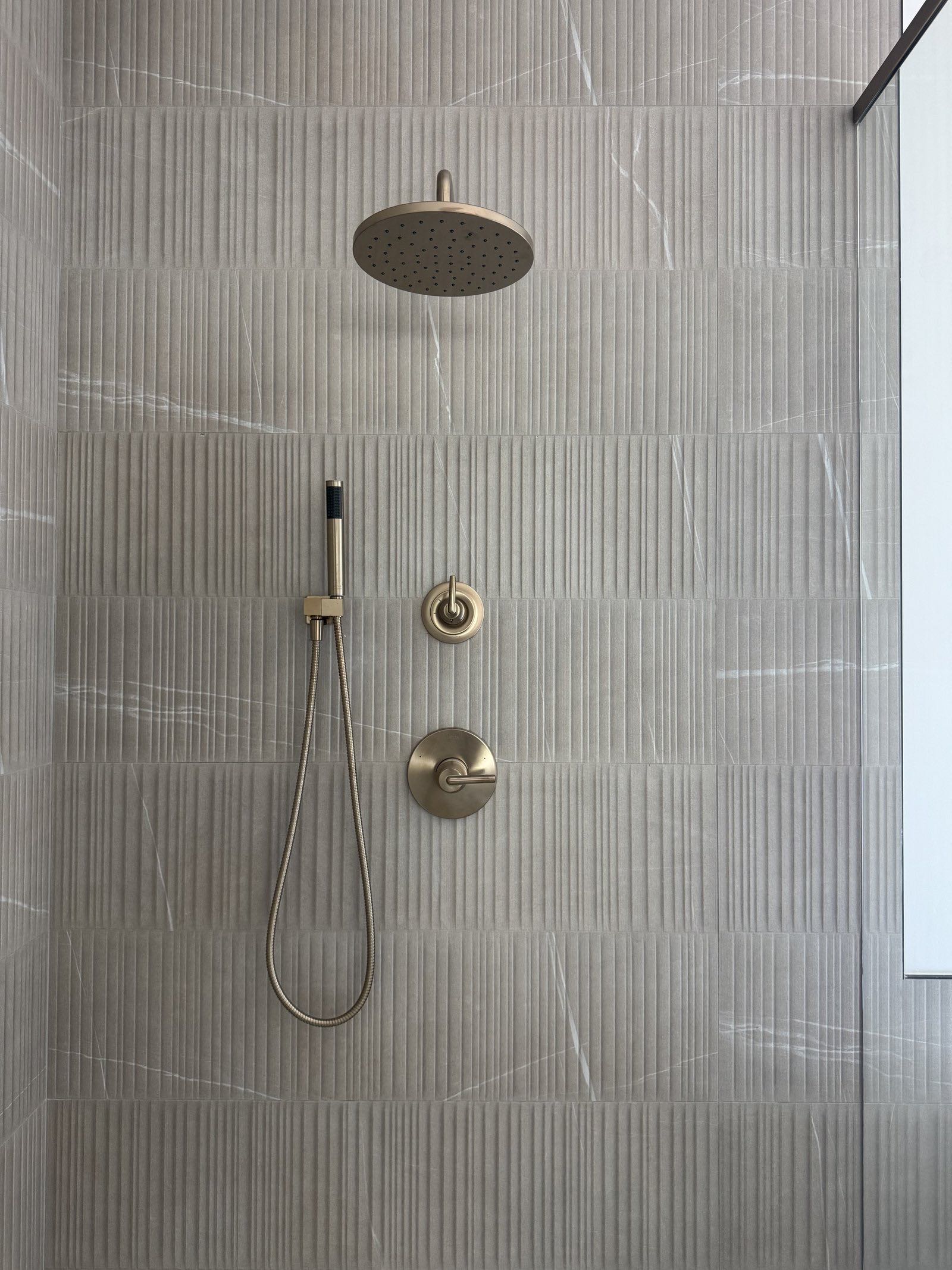 Close view of fluted shower tile and brushed brass fixtures