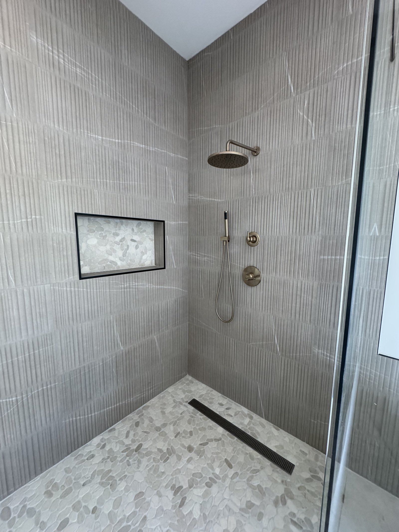Walk-in shower with textured neutral tile and brushed brass rain head
