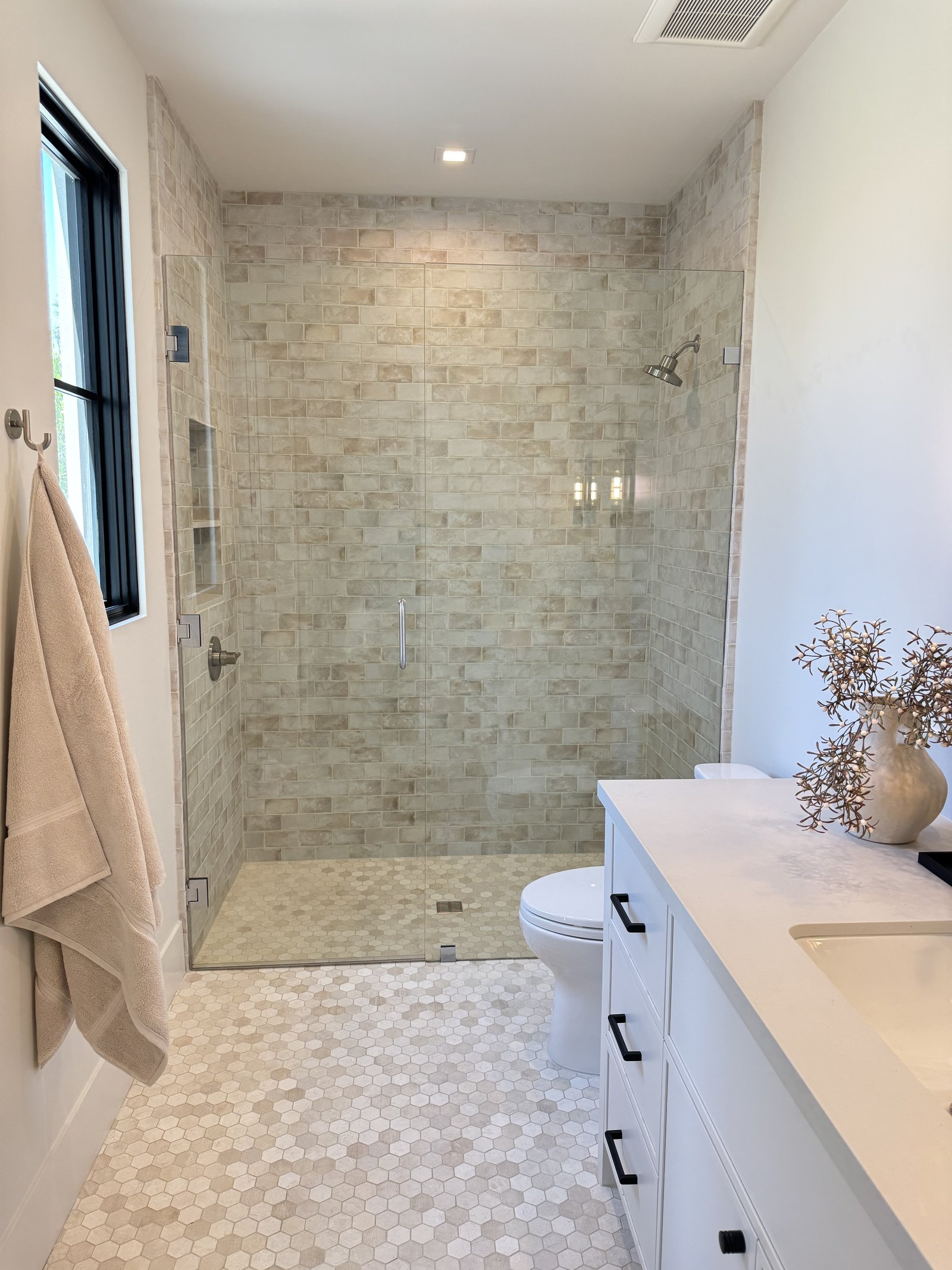 Mesa AZ bathroom remodel with beige natural-stone stacked subway shower, white shaker vanity, matte-black hardware, and hex marble floor