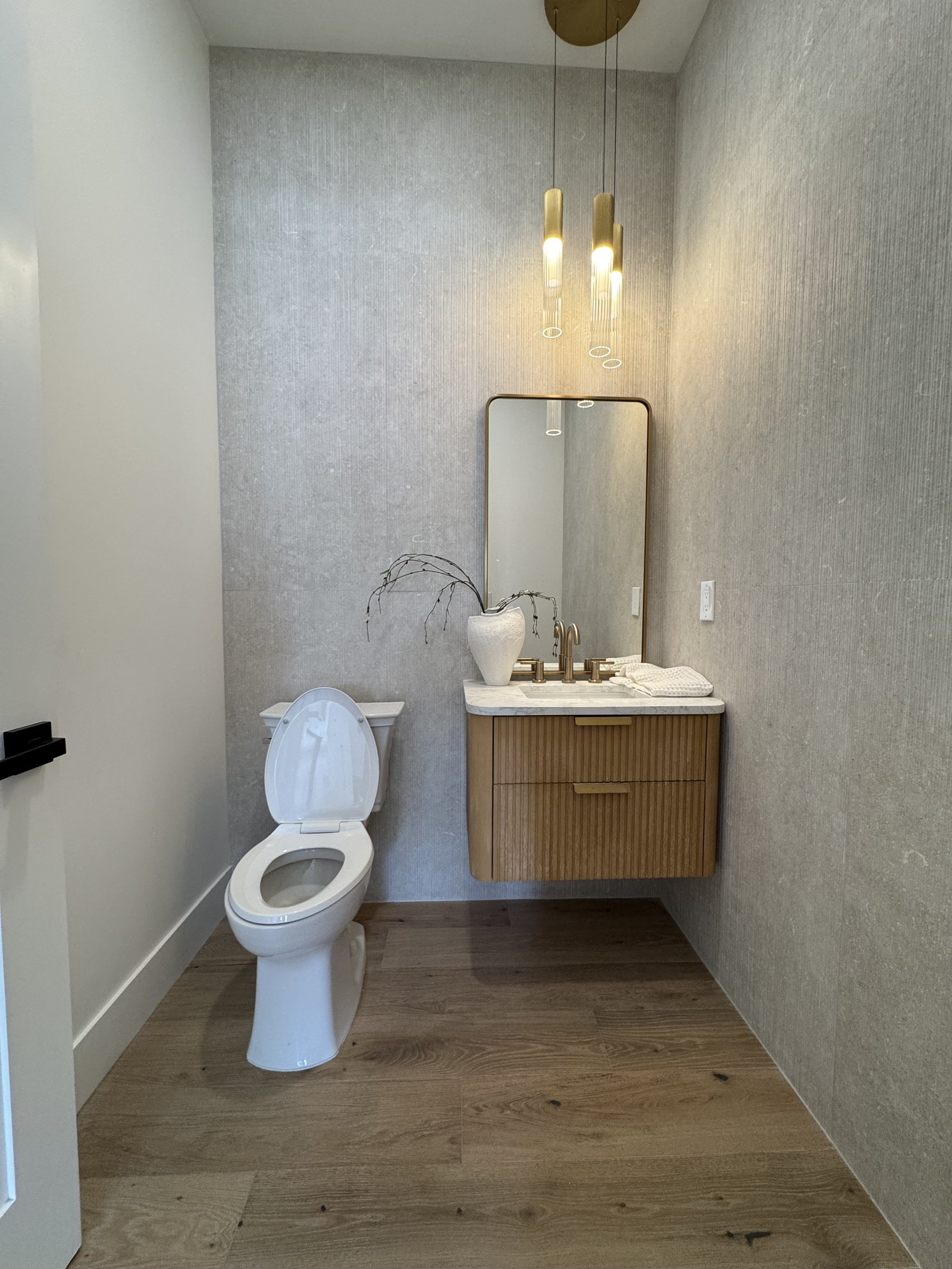 Queen Creek AZ powder room with fluted oak floating vanity, twin brass pendant lights, arched mirror, and grasscloth-style wallcovering