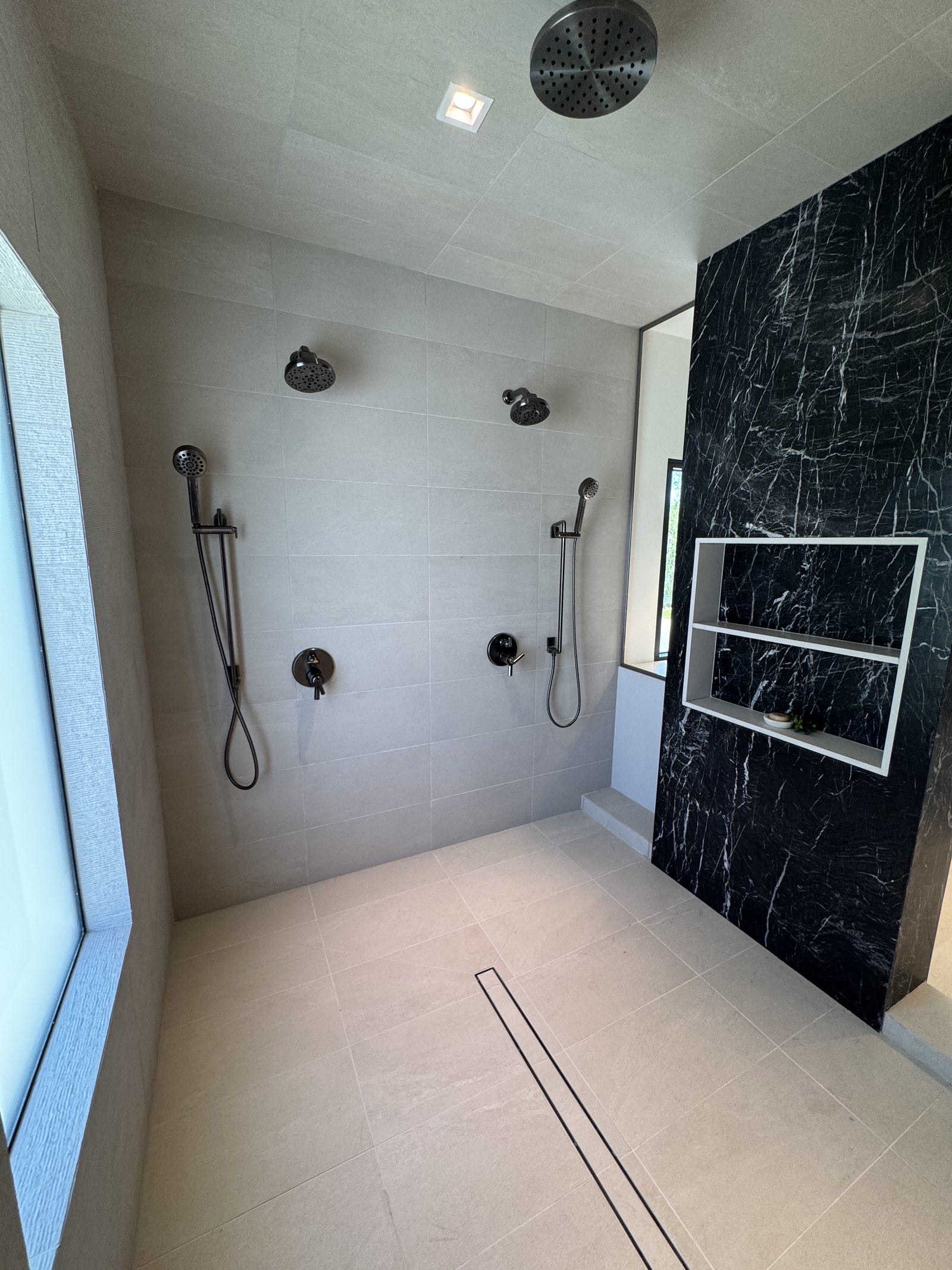 Large walk-in shower with black marble partition and multiple black fixtures