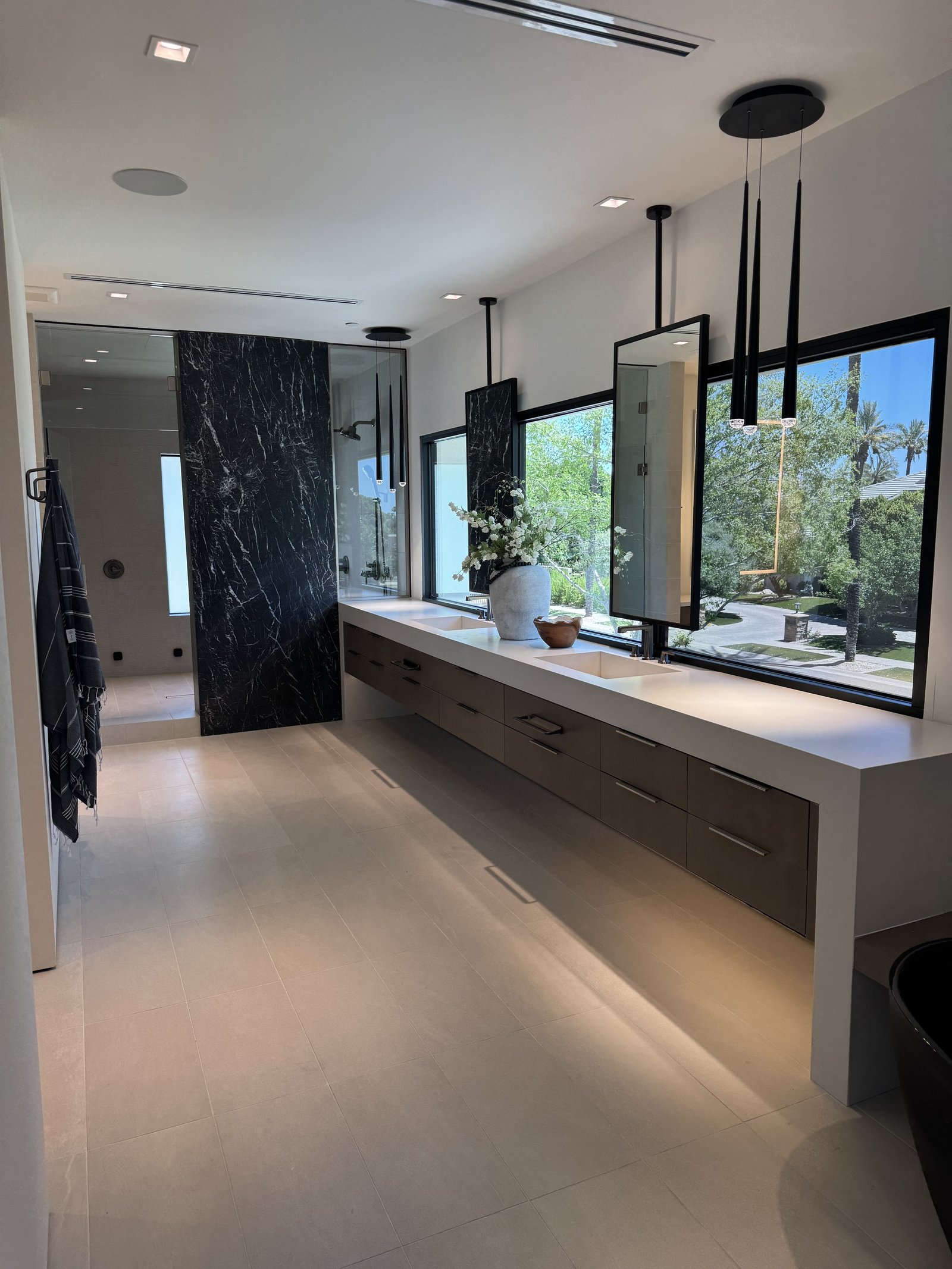 Scottsdale AZ primary bathroom with book-matched black marble waterfall partition wall, dark wood floating vanity with twin trough sinks, and black pendant lighting