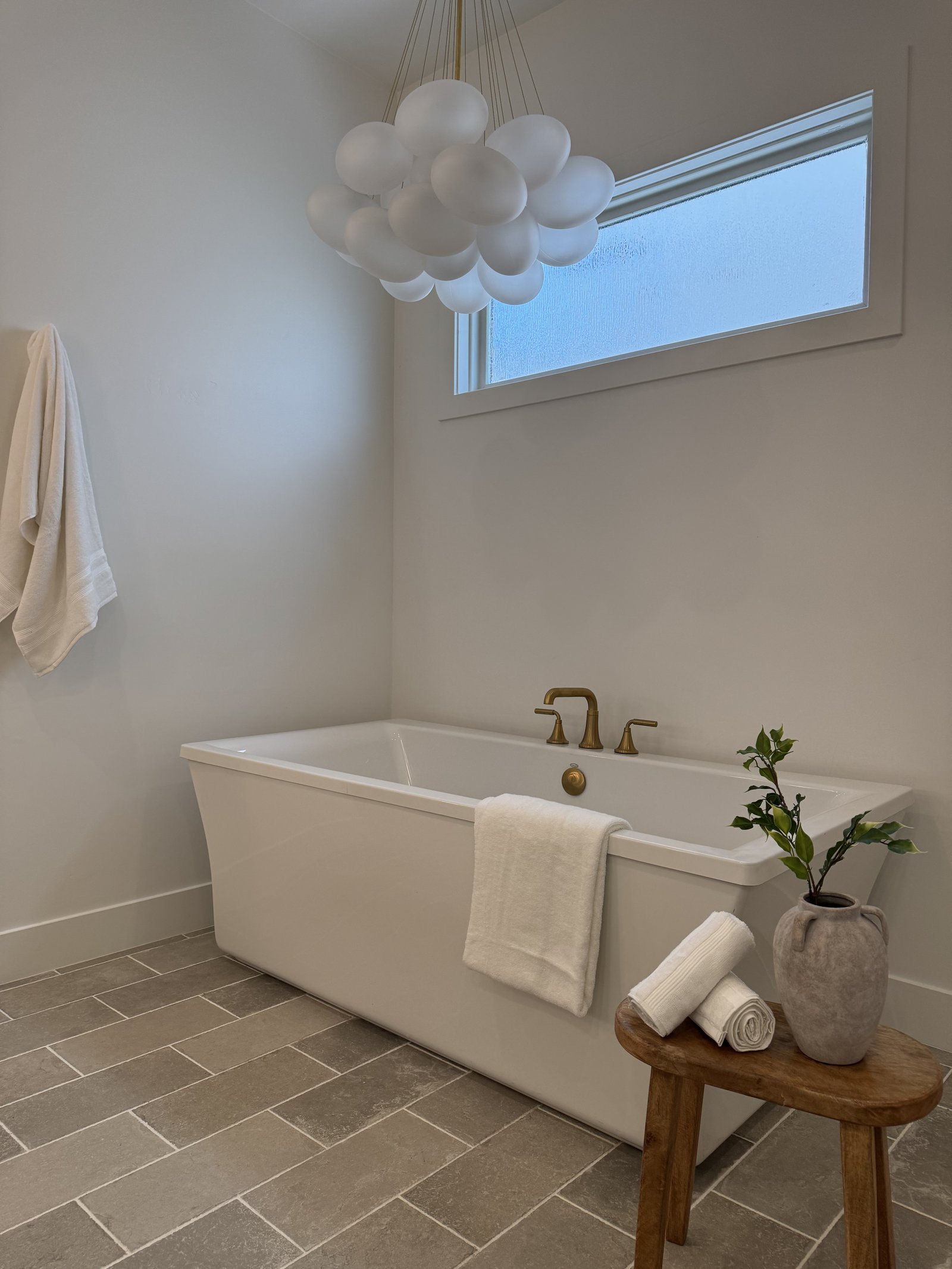 Scottsdale AZ luxury primary bathroom with freestanding tub, brass cluster pendant chandelier, brass tub filler, and travertine paver floor