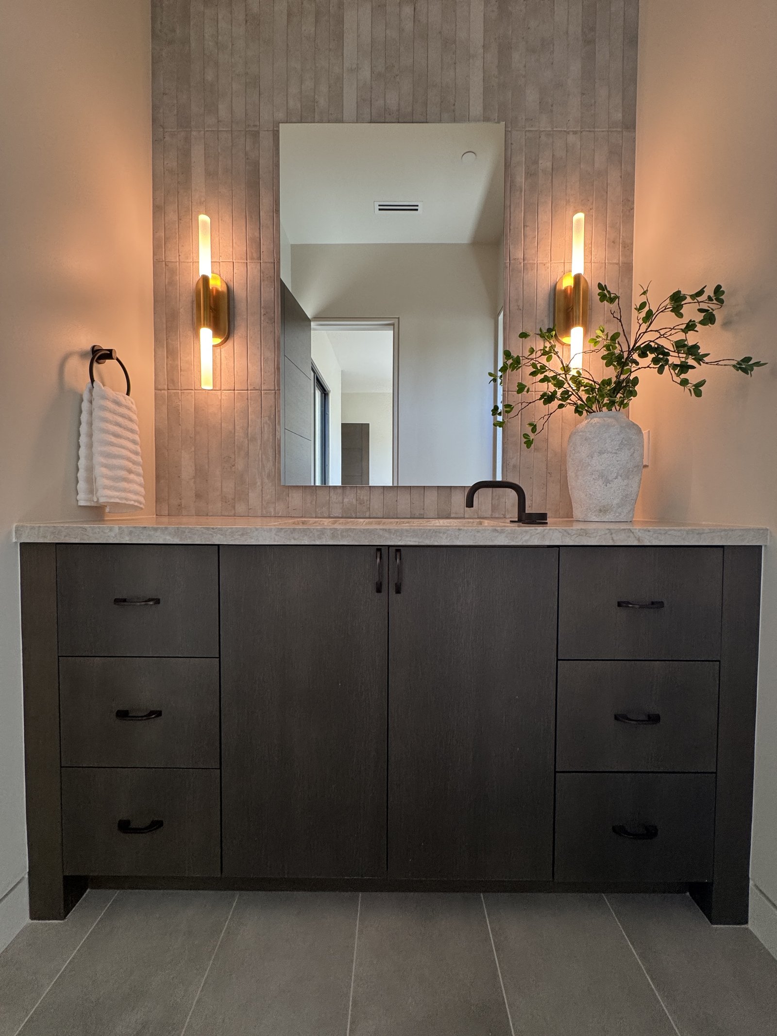 Floating dark wood bathroom vanity with dramatic stone counter and illuminated mirror