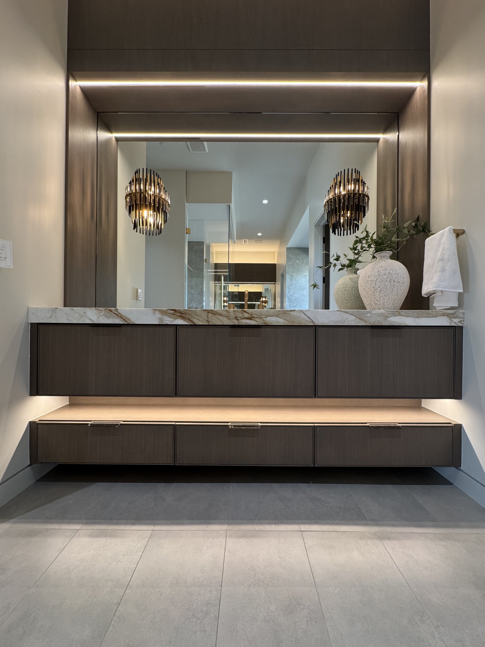 Dark wood floating vanity with stone top, sculptural sconces, and illuminated mirror