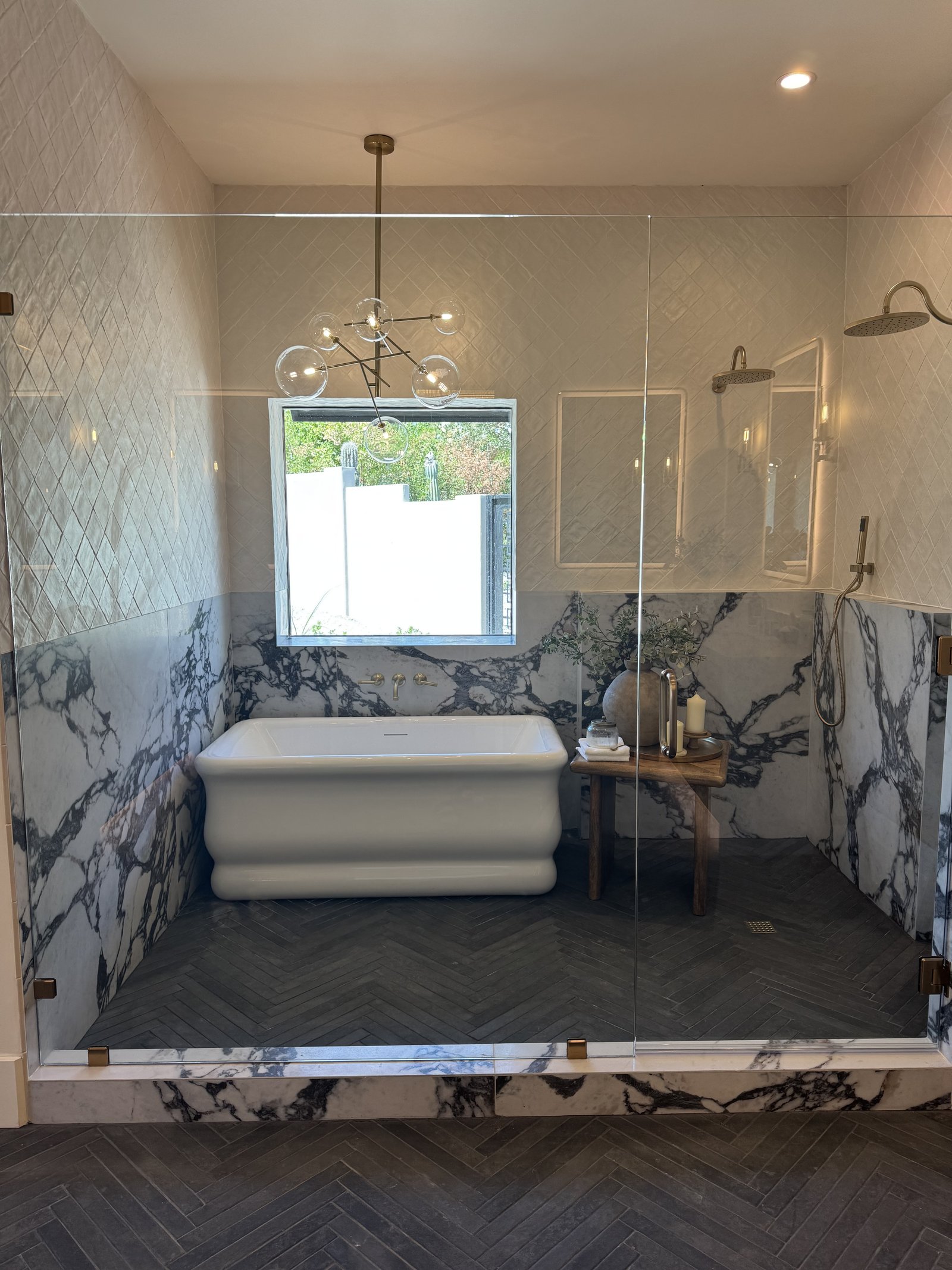 Scottsdale AZ primary bathroom with Calacatta Viola marble surround, sculptural freestanding tub, sputnik chandelier, and herringbone wood-look floor tile