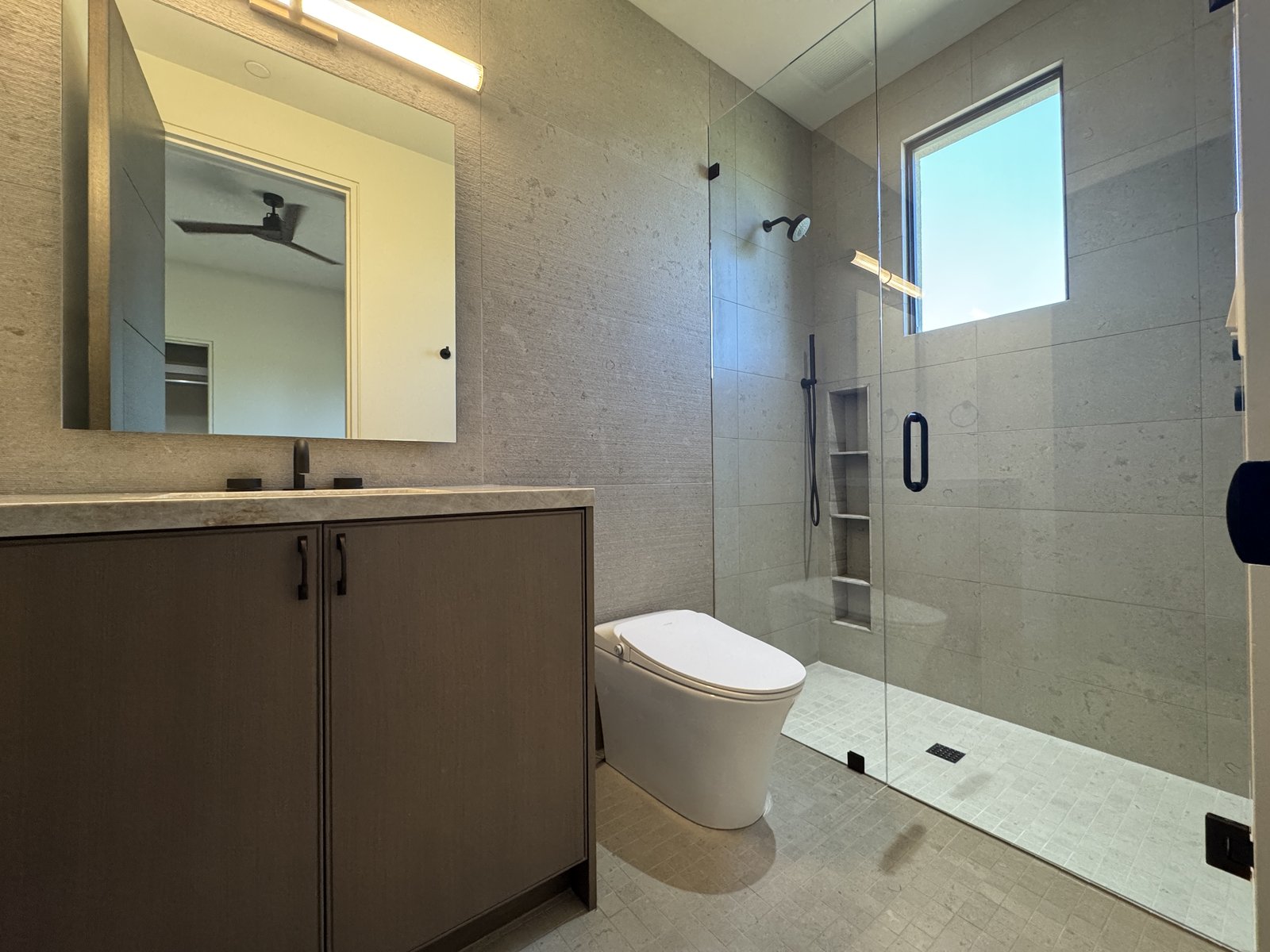 Tempe AZ compact bathroom remodel with textured stone-look tile shower, dark wood vanity, integrated lit medicine cabinet, and smart toilet