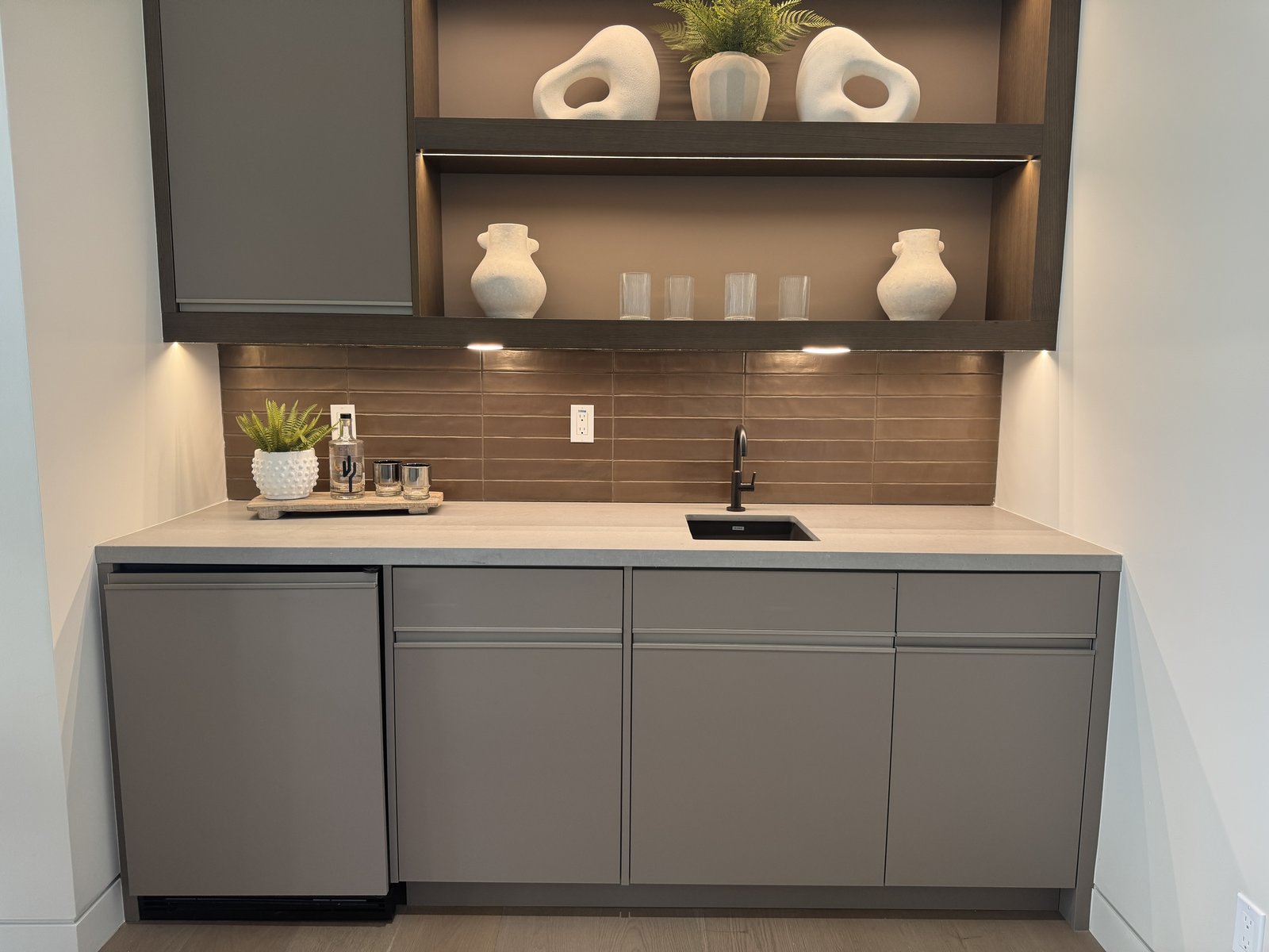 Scottsdale AZ custom home wet bar with flat-panel gray cabinetry, dark wood veneer back panel, white quartz counter, and integrated under-counter refrigeration