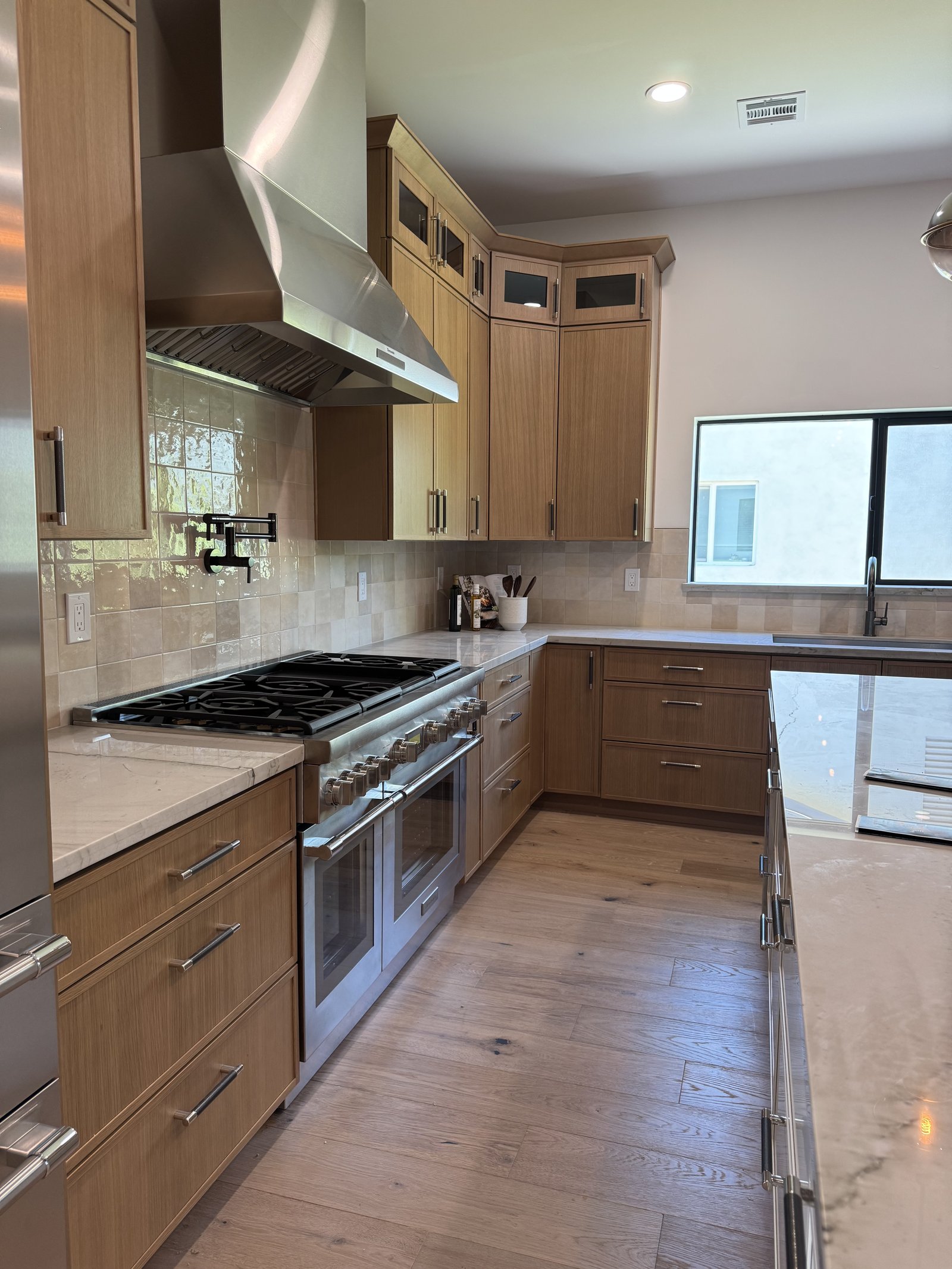 Natural modern kitchen remodel with light oak cabinetry to ceiling, marble countertops, stainless range hood, and brass pot filler in Chandler AZ